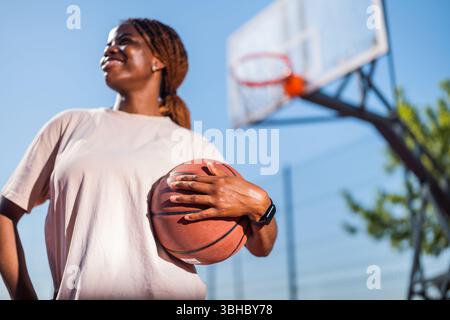 Jeune femme pratiquant le basket seule au terrain de sport le matin. Mise au point sélective sur la balle. Banque D'Images