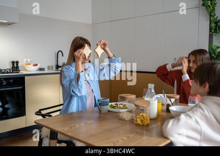 Maman ludique déjeunant avec des enfants montrant deux tranches de pain cachées aux enfants. Banque D'Images
