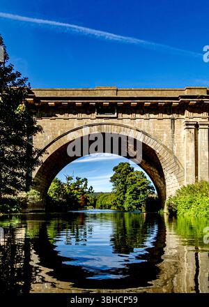Une vue pittoresque sur un pont en arc de pierre enjambant une rivière calme. Le pont, construit en pierre brun clair, dispose d'une grande arche centrale et déc Banque D'Images