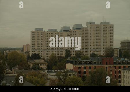 Paysage urbain couvert de Łódź, en Pologne, avec une vue dominante sur un grand bloc résidentiel emblématique de l'époque communiste surplombant d'anciens bâtiments en briques. Banque D'Images