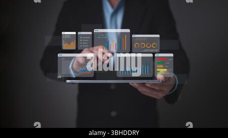 Homme d'affaires tenant une tablette affichant plusieurs diagrammes de données holographiques, symbolisant la veille économique complète, l'analyse des performances, un Banque D'Images
