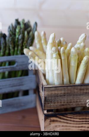 Asperges fraîches blanches et vertes soigneusement disposées dans une caisse en bois clair, parfaites pour cuisiner au printemps Banque D'Images