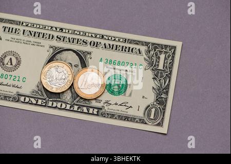 Un billet d'un dollar est affiché à côté de deux pièces d'Un pays différent, disposées soigneusement sur Une surface violette lisse. Les éléments contrastés Crea Banque D'Images