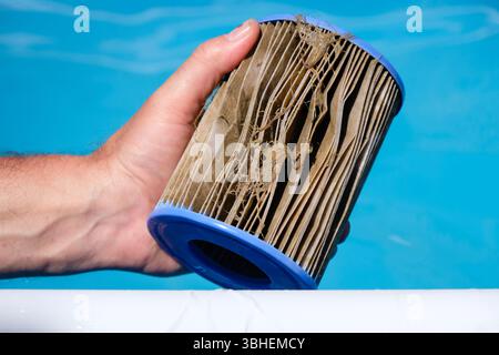 Cartouche filtrante de remplacement sale de piscine dans la main d'un homme. Substances pénétrant dans le filtre. Fond de piscine d'eau transparent. Copier l'espace. Banque D'Images
