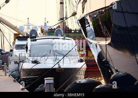 Un yacht club au coucher du soleil, des yachts et des voiliers sont amarrés aux couchettes, d'énormes défenses accrochées à des méga yachts, des cordes épaisses, des reflets sur les côtés brillants Banque D'Images