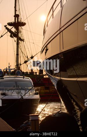 Un yacht club au coucher du soleil, des yachts et des voiliers sont amarrés aux couchettes, d'énormes défenses accrochées à des méga yachts, des cordes épaisses, des reflets sur les côtés brillants Banque D'Images