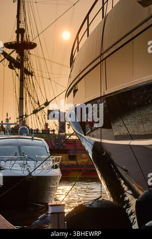 Un yacht club au coucher du soleil, des yachts et des voiliers sont amarrés aux couchettes, d'énormes défenses accrochées à des méga yachts, des cordes épaisses, des reflets sur les côtés brillants Banque D'Images
