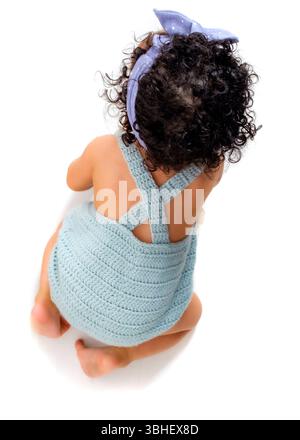Un bébé portant une barboteuse tricotée bleu clair et un bandeau à pois pervenches rampent sur le sol. Banque D'Images
