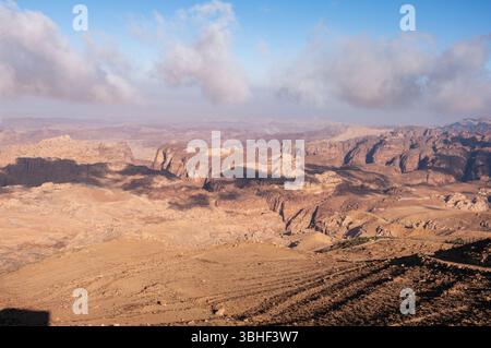 Un paysage désertique avec un ciel nuageux en arrière-plan. Le ciel est généralement clair, mais il y a quelques nuages dispersés partout. Le paysage est barr Banque D'Images