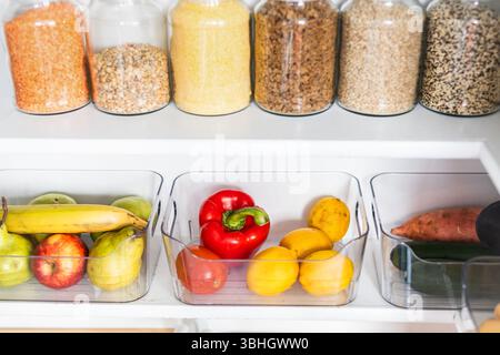 petit garde-manger organisé avec des bocaux transparents assortis remplis de céréales, légumineuses, épices et produits frais dans des récipients, alimentation saine, maison rangée, organi Banque D'Images