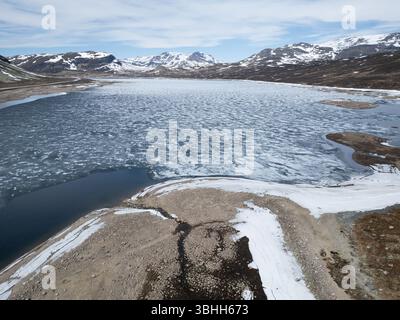 Vue aérienne d'un lac de montagne avec glace fondante au printemps, Norvège. Prise de vue par drone d'un paysage scandinave rude avec de la neige sur les sommets. Banque D'Images