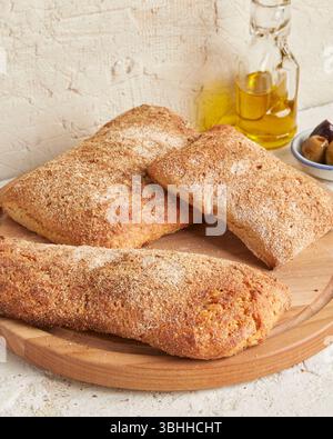 Ciabatta d'épeautre sur une surface en bois avec des olives et de l'huile d'olive en arrière-plan - un pain rustique de style méditerranéen, parfait pour l'apéritif. Banque D'Images