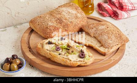 Ciabatta d'épeautre sur une surface en bois avec des olives et de l'huile d'olive en arrière-plan - un pain rustique de style méditerranéen, parfait pour l'apéritif. Banque D'Images