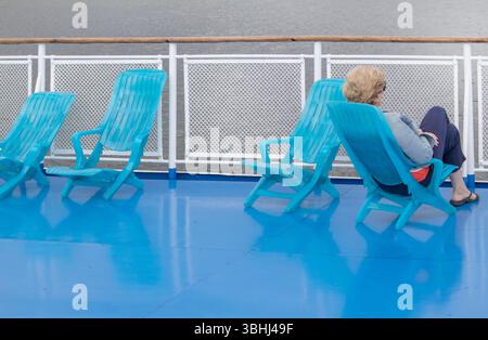 Une femme solitaire d'âge moyen est assise dans une chaise longue sur le pont d'un bateau de croisière, regardant vers la mer. Visage méconnaissable Banque D'Images