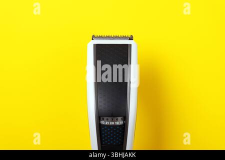 Gros plan d'une tondeuse à cheveux électrique moderne sur fond jaune vif, présentant des outils de toilettage et des équipements de soins personnels. Banque D'Images