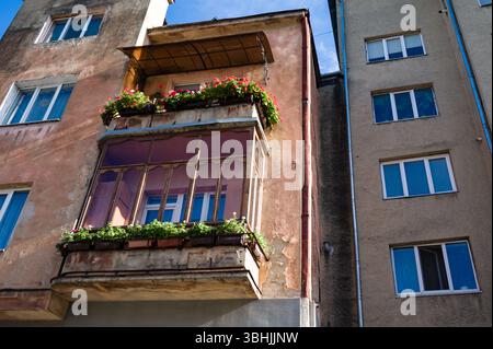 Un bâtiment altéré présente un joli balcon débordant de fleurs colorées, contrastant avec les structures voisines sous un bleu brillant s. Banque D'Images