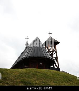 Vue d'une chapelle en bois et clocher d'en bas sur une colline herbeuse dans le village de Drvengrad. Mokra Gora, pays de Serbie. Banque D'Images
