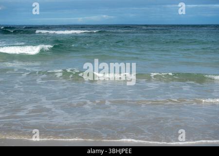 Les vagues douces roulent et se brisent doucement sur une plage de sable, capturant le rythme apaisant de l'océan, idéal pour les thèmes de la tranquillité, de la nature, du beau littoral Banque D'Images