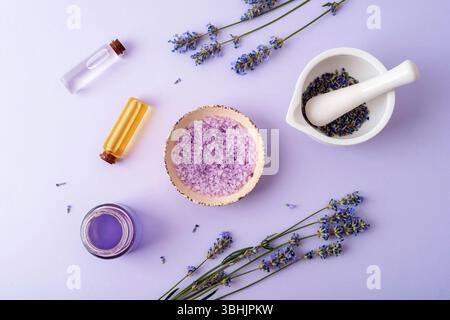 Sel de bain de lavande dans un bol, mortier et pestel avec des fleurs de lavande, huile d'arôme et hydrolat sur fond violet. Médecine des herbes naturelles, arôme Banque D'Images
