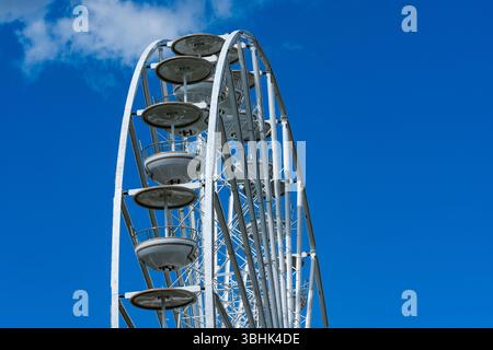 La structure imposante d'une grande roue se dresse bien en évidence contre un ciel bleu clair. Ses cabanes emblématiques sont visibles, invitant les visiteurs à profiter d'un scen Banque D'Images
