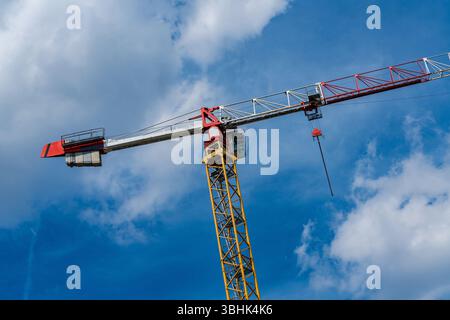 Une grande grue de construction se tient bien en vue contre un ciel bleu vif rempli de nuages blancs moelleux. Ses couleurs vives rouge et jaune se démarquent, s Banque D'Images