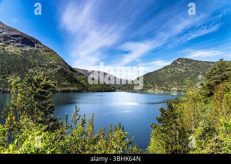 Une vue imprenable sur un lac de montagne tranquille entouré de collines verdoyantes et de sommets enneigés sous un ciel bleu clair, évoquant des sentiments de paix, Ser Banque D'Images