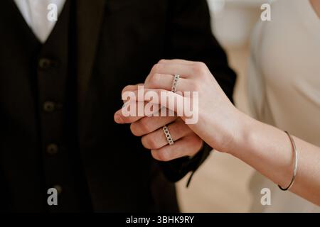 Jeune homme adulte caucasien et jeune femme adulte caucasienne se tenant la main pendant la célébration de mariage, tous deux portant des anneaux de mariage Banque D'Images