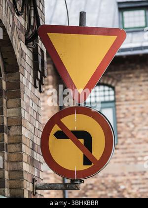 Deux panneaux de signalisation routière sont bien en vue sur un bâtiment en Suède. Un panneau indique aux conducteurs de céder, tandis que l'autre interdit les virages à gauche. L'urbain Banque D'Images