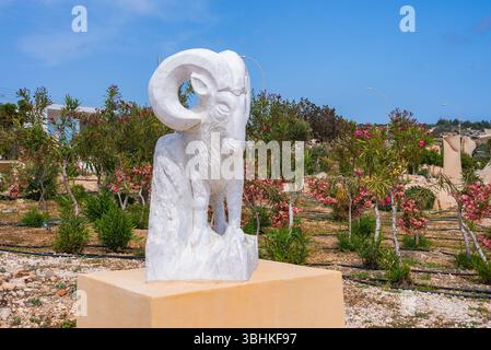 Statue de RAM en marbre blanc dans un jardin avec des arbustes à fleurs roses Banque D'Images
