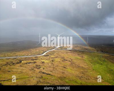 Tir par drone d'éoliennes sous un arc-en-ciel vibrant avec la pluie approchant - nature et énergie renouvelable en harmonie dynamique. Banque D'Images