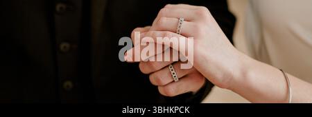 Jeune homme adulte caucasien et jeune femme adulte caucasienne se tenant par la main pendant la célébration de mariage, tous deux portant des anneaux de mariage, gros plan des mains montrant l'engagement et l'unité Banque D'Images