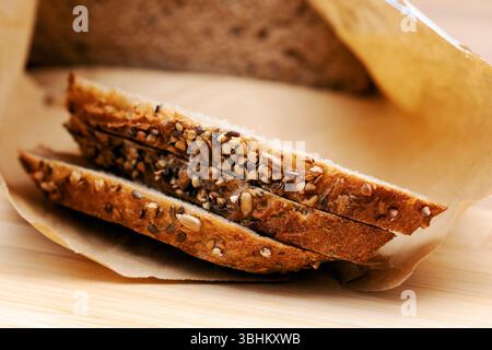 Gros plan de plusieurs tranches de pain rustique au levain, généreusement recouvertes de diverses graines, reposant sur du papier parchemin Banque D'Images