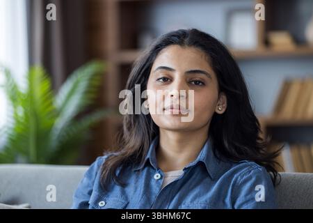 Un portrait d'une femme attrayante de couleur regardant directement la caméra tout en se relaxant à l'intérieur avec un fond naturel. Banque D'Images