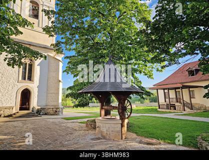 Vieux puits traditionnel en bois et pierre et le clocher entouré de vieux chênes dans la cour du monastère de Capriana, République de Moldavie Banque D'Images
