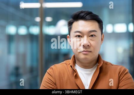 Portrait d'un homme asiatique regardant directement la caméra avec une expression sérieuse. Il porte une chemise marron. Banque D'Images