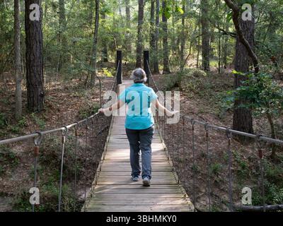 Femme âgée active marchant sur un pont suspendu en bois dans la forêt d'État W. G. Jones au Texas. Photographié dos à la caméra. Banque D'Images