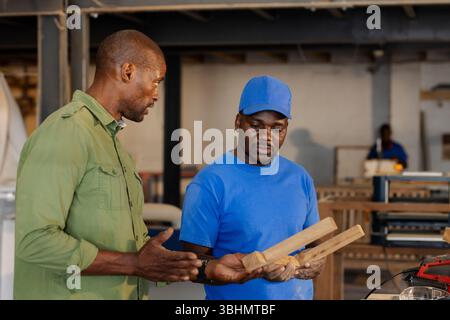 Collègues afro-américains inspectant et discutant des planches de bois à l'atelier avec scie à table Banque D'Images