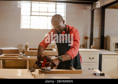 Ponceuse électrique à main glissant sur une planche de bois sur un établi robuste dans un atelier avec lumière naturelle Banque D'Images