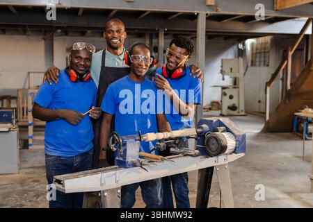Hommes afro-américains travaillant autour du tour à bois avec des ciseaux portant des lunettes de sécurité à l'intérieur de l'atelier Banque D'Images