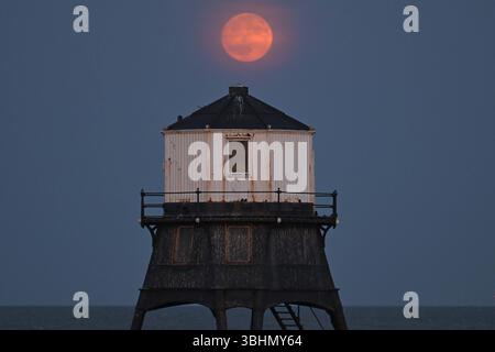 Pleine lune de fraise la pleine lune de fraise se lève au-dessus du phare inférieur de Dovercourt Essex UK. La pleine Lune est assise bas sur l'horizon sud donnant l'illusion d'une Lune surdimensionnée causée par ce que l'on appelle un arrêt lunaire majeur qui se produit tous les 18,6 ans. Essex Dovercourt UK Copyright : xMartinxDaltonx Strawberry Moon 100624 MD 212 Banque D'Images