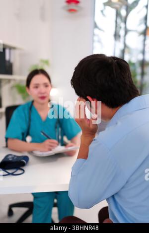 Médecin féminin adulte asiatique dans les gommages bleus consulte un patient concerné éprouvant un mal de tête lors d'un bilan fournit des conseils et un traitement opti Banque D'Images