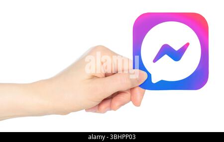 La main tient en papier l'icône de l'application mobile Facebook Messenger, sur un fond transparent. Facebook Messenger est une application de messagerie instantanée propriétaire américaine Banque D'Images