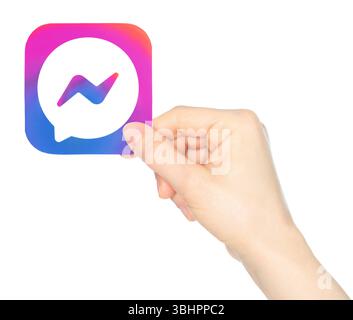 La main tient en papier l'icône de l'application mobile Facebook Messenger, sur un fond transparent. Facebook Messenger est une application de messagerie instantanée propriétaire américaine Banque D'Images