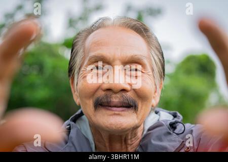 Portrait en gros plan d'un homme asiatique aîné prenant un selfie, souriant à l'appareil photo à l'extérieur avec mobile intelligent, appareil téléphonique. Concept mobile et technologique. Banque D'Images