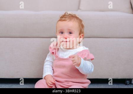 Teary eyed Baby Girl est assis sur la moquette avant le canapé beige, pointant à la recherche de confort. Banque D'Images