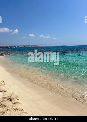 Le sable doré rencontre des eaux turquoises cristallines sous un ciel bleu vif. Une scène de plage paisible parfaite pour l'été, les voyages ou les thèmes de vacances. Banque D'Images