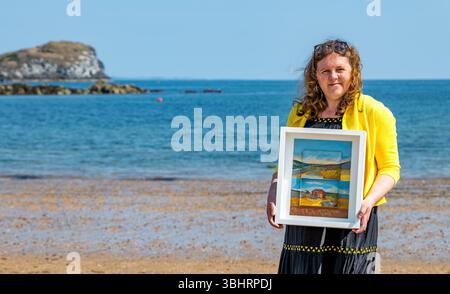 North Berwick, East Lothian, Écosse, Royaume-Uni, 11 juin 2025. Préparation pour l'exposition : L'artiste Jayne Stokes, spécialisée dans les peintures de paysages miniatures sur les « objets trouvés » tels que les boîtes d'allumettes, les vieilles boîtes de conserve ou la poterie de mer, se prépare pour l'ouverture de son exposition à Open Eye Gallery. L'exposition se concentre sur les peintures des Shetland : elle a reçu le prix VACMA Creative Scotland Artists Bursary Award pour y voyager cette année. Pic : Jayne avec un de ses tableaux sur la plage. Crédit : Sally Anderson/Alamy Live News Banque D'Images