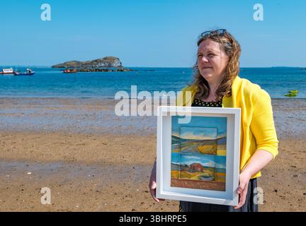North Berwick, East Lothian, Écosse, Royaume-Uni, 11 juin 2025. Préparation pour l'exposition : L'artiste Jayne Stokes qui se spécialise dans les peintures de paysage miniatures sur les objets trouvés tels que les boîtes d'allumettes, les vieilles boîtes de conserve ou la poterie de mer, se prépare pour l'ouverture de son exposition à Open Eye Gallery. L'exposition se concentre sur les peintures des Shetland : elle a reçu le prix VACMA Creative Scotland Artists Bursary Award pour y voyager cette année. Pic : Jayne avec un de ses tableaux sur la plage. Crédit : Sally Anderson/Alamy Live News Banque D'Images