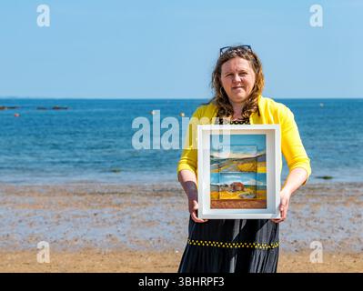 North Berwick, East Lothian, Écosse, Royaume-Uni, 11 juin 2025. Préparation pour l'exposition : L'artiste Jayne Stokes, spécialisée dans les peintures de paysages miniatures sur les « objets trouvés » tels que les boîtes d'allumettes, les vieilles boîtes de conserve ou la poterie de mer, se prépare pour l'ouverture de son exposition à Open Eye Gallery. L'exposition se concentre sur les peintures des Shetland : elle a reçu le prix VACMA Creative Scotland Artists Bursary Award pour y voyager cette année. Pic : Jayne avec un de ses tableaux sur la plage. Crédit : Sally Anderson/Alamy Live News Banque D'Images