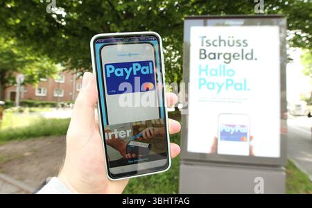 Anti-Bargeld-Werbung auf einer Werbetafel von Ströer vom Online-Bezahldienst PayPal. DAS Unternehmen wirbt aktuell in Deutschland großspurig für die Möglichkeit, mit seiner App kontaklos zu zahlen. Davor hält ein Mann ein smartphone in der hand, auf dem die website von PayPal geöffnet ist. Dort informiert das Unternehmen über die Möglichkeit des kontaklosen Zahlens. Barmbek Hambourg *** publicité anti-cash sur un panneau d'affichage Ströer du service de paiement en ligne PayPal la société annonce actuellement la possibilité de payer sans contact avec son application en Allemagne dans le grand style devant Banque D'Images